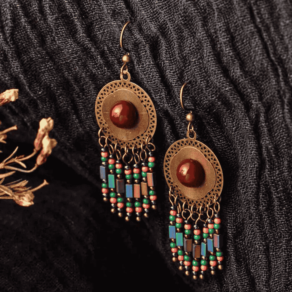 Pair of ornate earrings with beads on a textured black fabric background