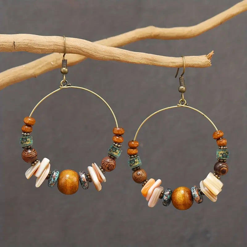 Hoop earrings with bead and shell decorations on a branch against a gray background