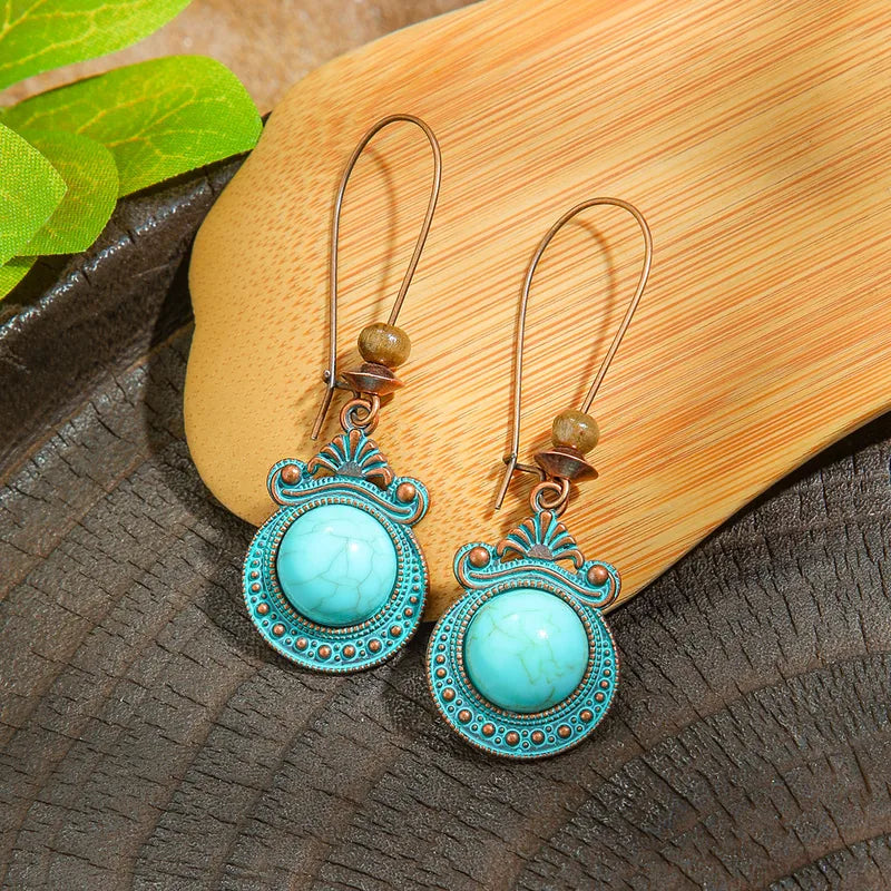Pair of turquoise earrings with decorative metalwork on a wooden surface.