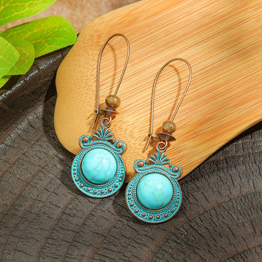 Pair of turquoise earrings with decorative metalwork on a wooden surface.