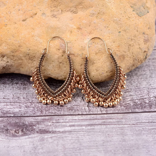 Pair of gold hoop earrings with bead details on a stone and wooden surface