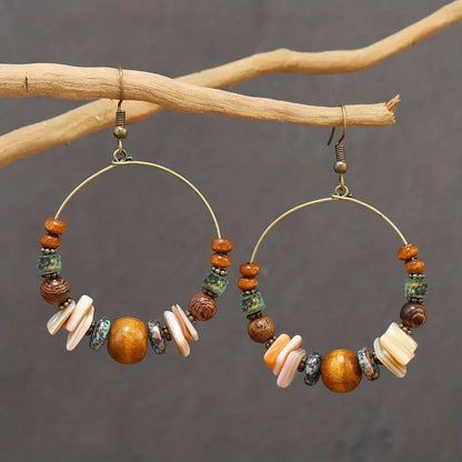 Hoop earrings with bead and shell decorations on a branch against a gray background