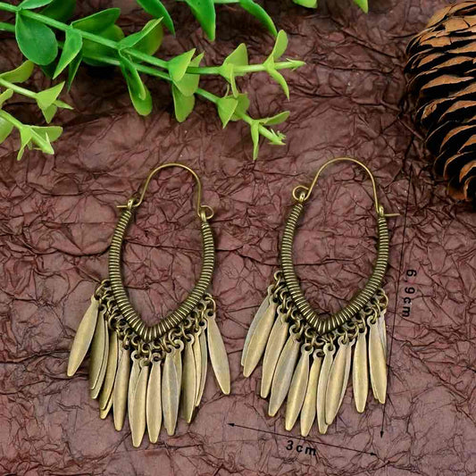 A pair of gold dangler earrings with an elegant design, displayed against a natural backdrop with green leaves and a pine cone.