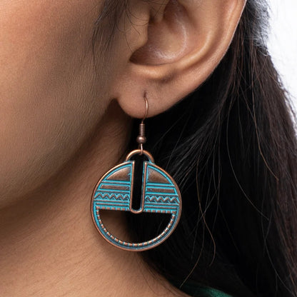 Close-up of an ear wearing a turquoise and bronze earring with geometric design.